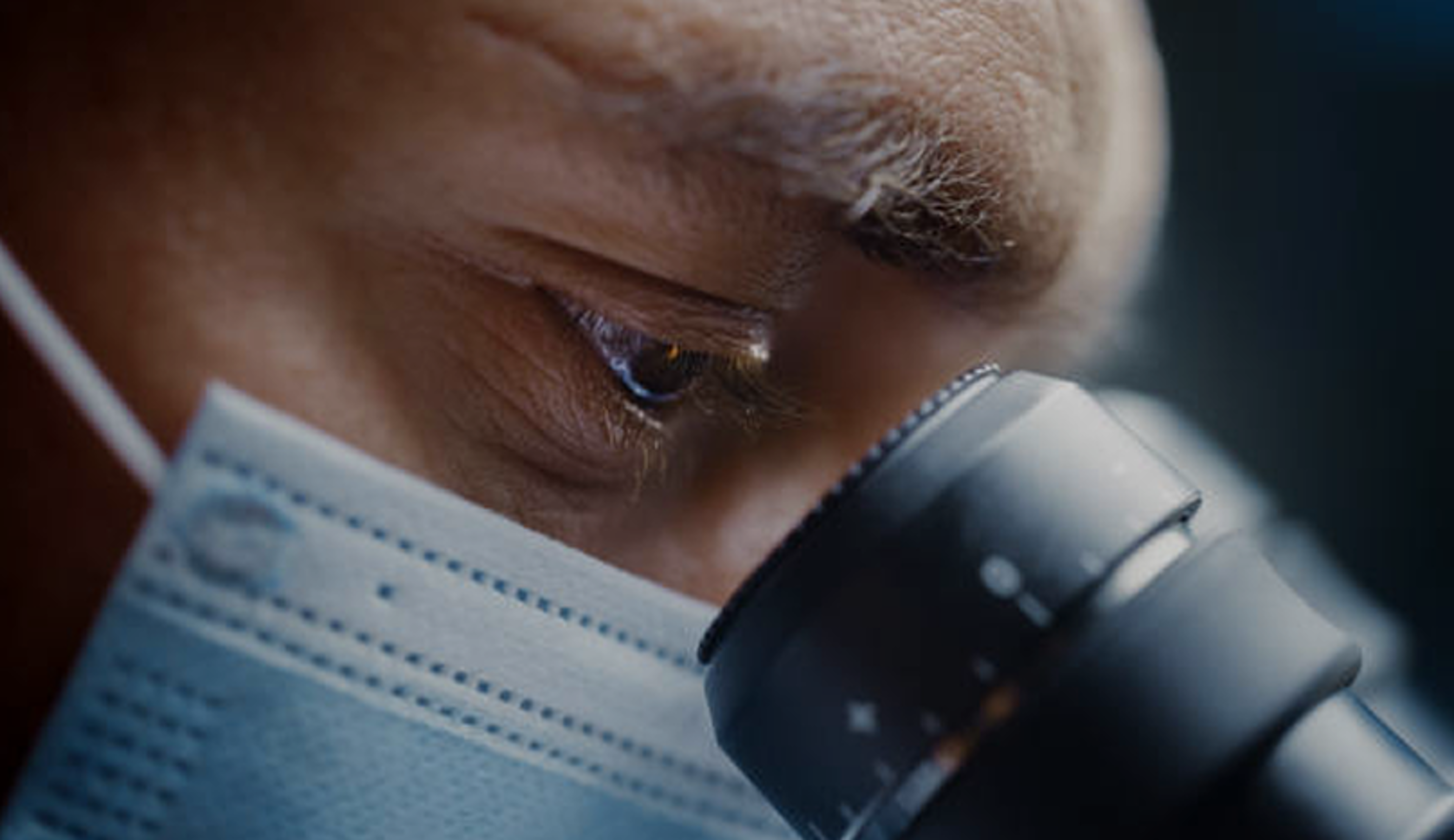 Scientist wearing surgical mask and looking into microscope.png