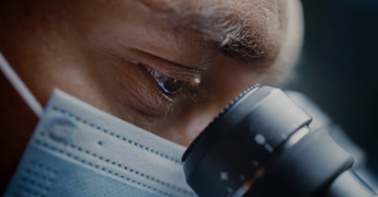 Scientist wearing surgical mask and looking into microscope.png